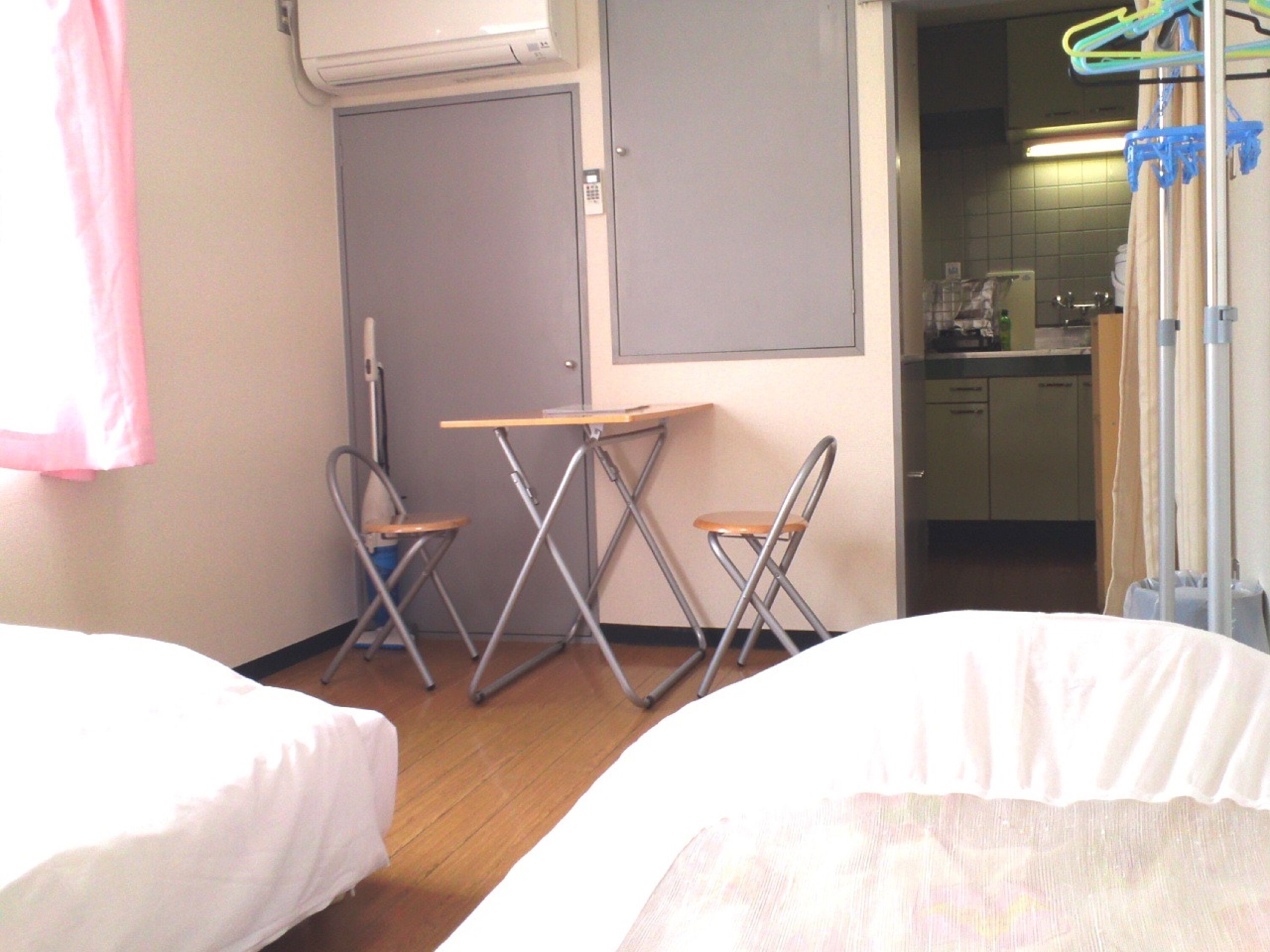 A hotel room with two beds, a small table, two foldable chairs, a door, and a view into the kitchen area.