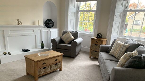 Een woonkamer met een grijze bank, een houten salontafel, een grijze fauteuil en een klein bijzettafeltje.