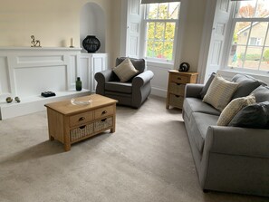 Un salon avec un canapé gris, une table basse en bois, un fauteuil gris et une petite table d’appoint en bois.