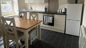 Een keuken met witte kastjes, een zwart aanrecht, een fornuis, een magnetron en een koelkast.