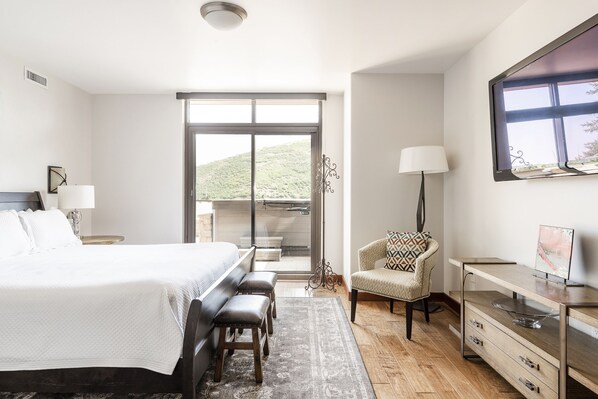 Un dormitorio moderno con una cama grande, un escritorio, una silla y vistas a una colina.