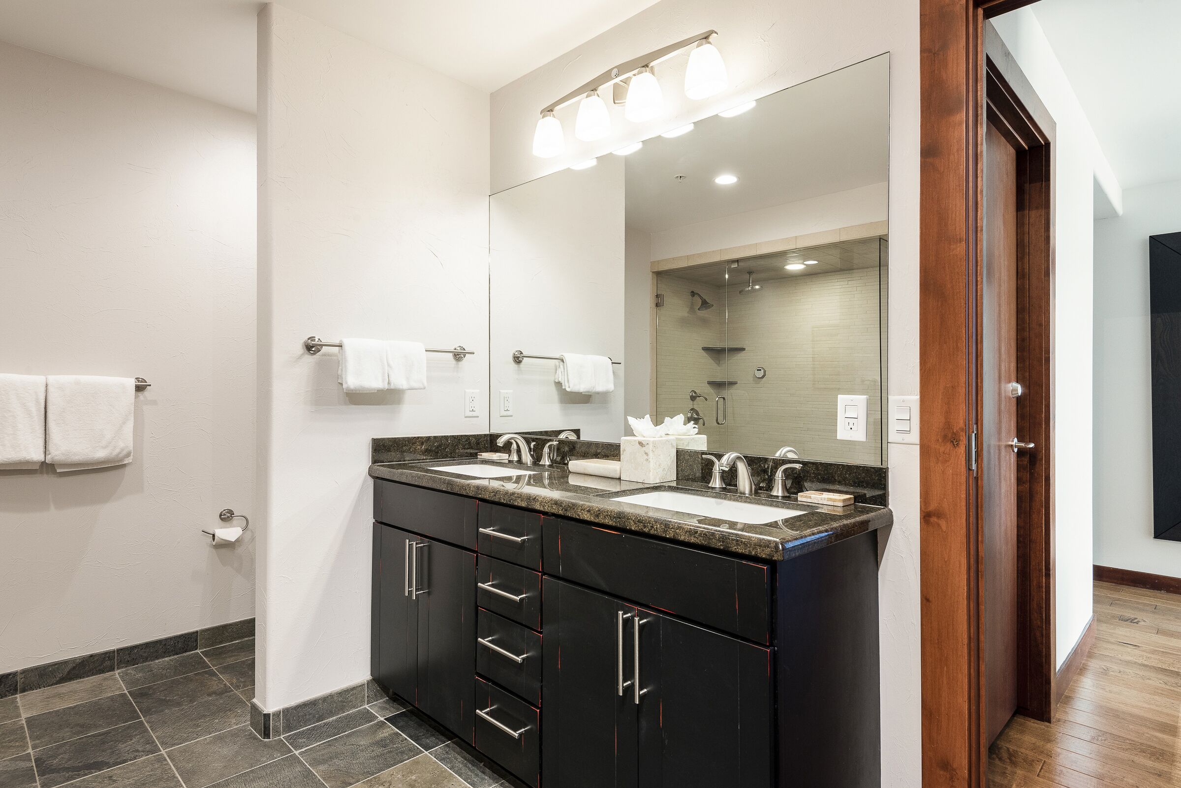 A modern bathroom with two sinks, a large mirror, and a shower area.