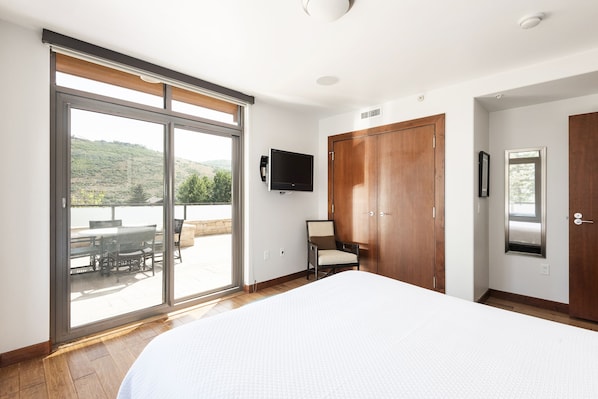 Ein Schlafzimmer mit einem großen Bett, einer Schiebetür zu einer Terrasse, einem an der Wand befestigten Fernseher und Holzschränken.