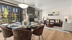 A modern living room with a dining area, large windows, and a fireplace.