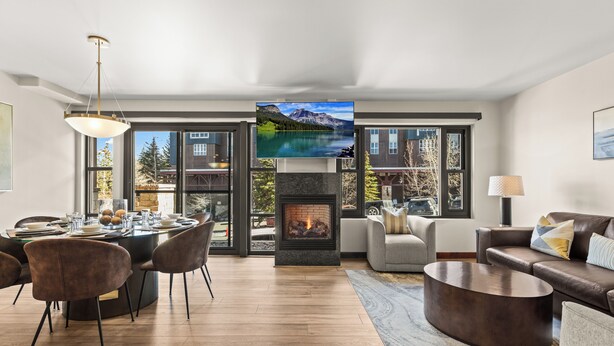 A modern living room with a fireplace, a dining area, and large windows offering a mountain view.