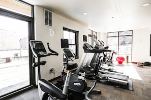 A gym with various exercise equipment, large windows, and a view of the outside.