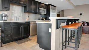 A modern kitchen with dark cabinetry, stainless steel appliances, and a central island with stools. - Managed by Park City Lodging-Luxury 2 Bdrm Ski-In/Ski-Out at Park City Mountain (Park City)