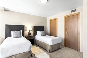 A hotel room with two beds, a nightstand with a lamp, a wooden wardrobe, and a carpeted floor.