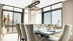A dining area with a large table set for six, surrounded by six upholstered chairs. The room has large windows offering a view of a snowy landscape. - Managed by Park City Lodging-Luxury 2 Bdrm Ski-In/Ski-Out at Park City Mountain (Park City)