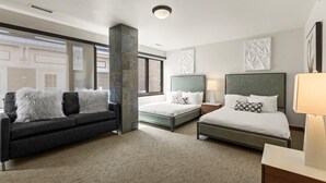 Quarto de hotel com uma janela grande, um sofá, duas camas e uma mesa de cabeceira.
