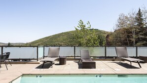Uma piscina no terraço com espreguiçadeiras e vista para uma colina.
