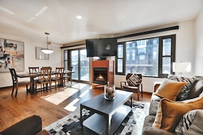 A modern living room with a fireplace, dining area, and large windows.