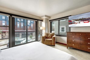Spacious king bedroom with large windows, comfortable seating, a dresser, and TV.