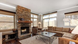 A modern living room with a stone fireplace, large windows, and a cozy seating area.