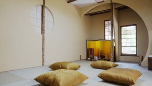 Un espacio tradicional con esteras de tatami, cuatro cojines, un celosía de papel y techo con vigas de madera.