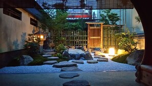 A traditional Japanese garden with a stone pathway leading to a wooden gate, surrounded by rocks and greenery. - Sanjyo PREMIUM (Kyoto)