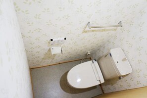 A bathroom with a toilet, a paper towel dispenser, and a hand dryer on the wall.