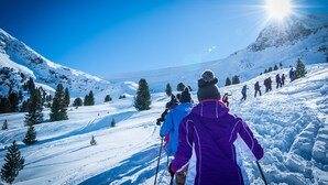 A snowy mountain landscape with skiers and a clear blue sky.