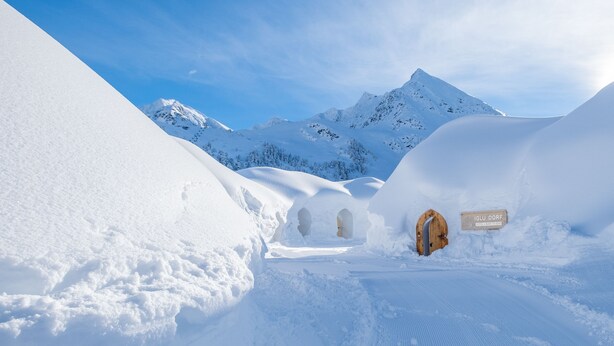 A snow-covered landscape with a wooden structure and a sign that reads "IGLU DORF."