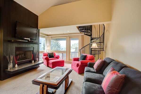 A living room with a fireplace, red and black sofas, a glass coffee table, and a black spiral staircase. - Mountain Summit Getaway - within minutes of Alta and Snowbird (Alta)