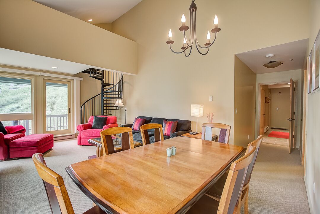 A spacious living area with a wooden dining table, red and black sofas, and a staircase leading to an upper level.