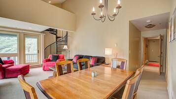 A spacious living area with a wooden dining table, red and black sofas, and a staircase leading to an upper level.
