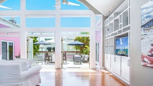 A spacious room with a white sofa, a TV, and a view of the outdoors through large windows. - Rooftop Penthouse (Key West)
