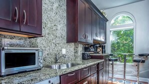 A kitchen with granite countertops, stainless steel appliances, dark wooden cabinets, and a window overlooking greenery. - Rooftop Penthouse (Key West)