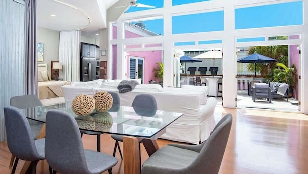 A modern living room with a glass dining table, grey chairs, and a white sofa. - Rooftop Penthouse (Key West)