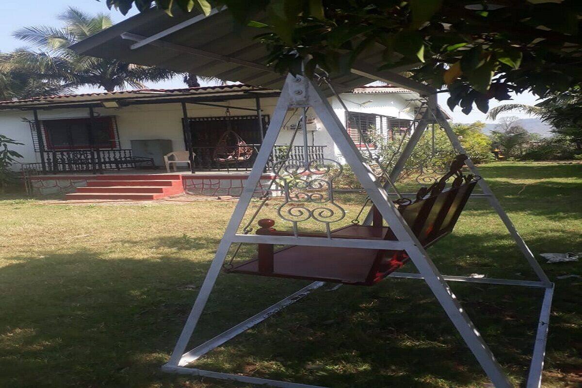 A swing chair under a tree, a house with a porch, and a grassy yard.