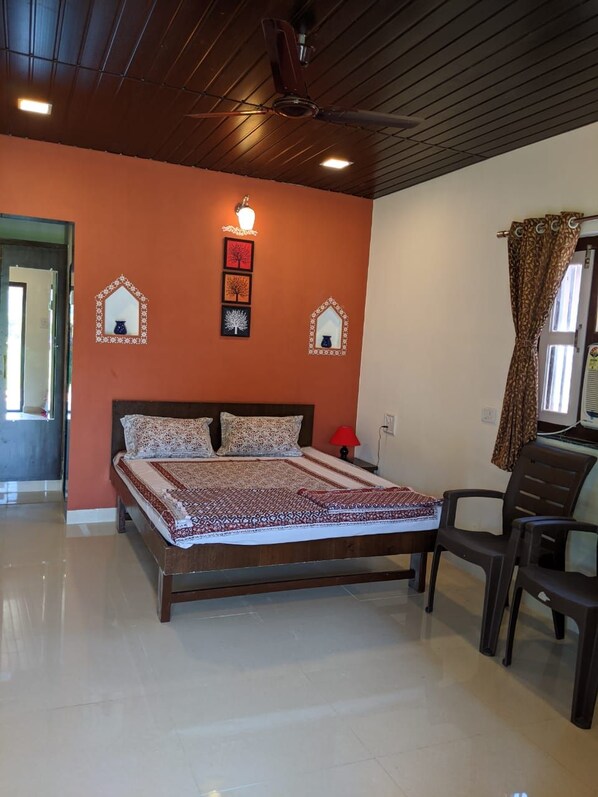A bedroom with a wooden bed, a ceiling fan, and a wall-mounted light fixture. - Mango Tree Farm (Karjat)