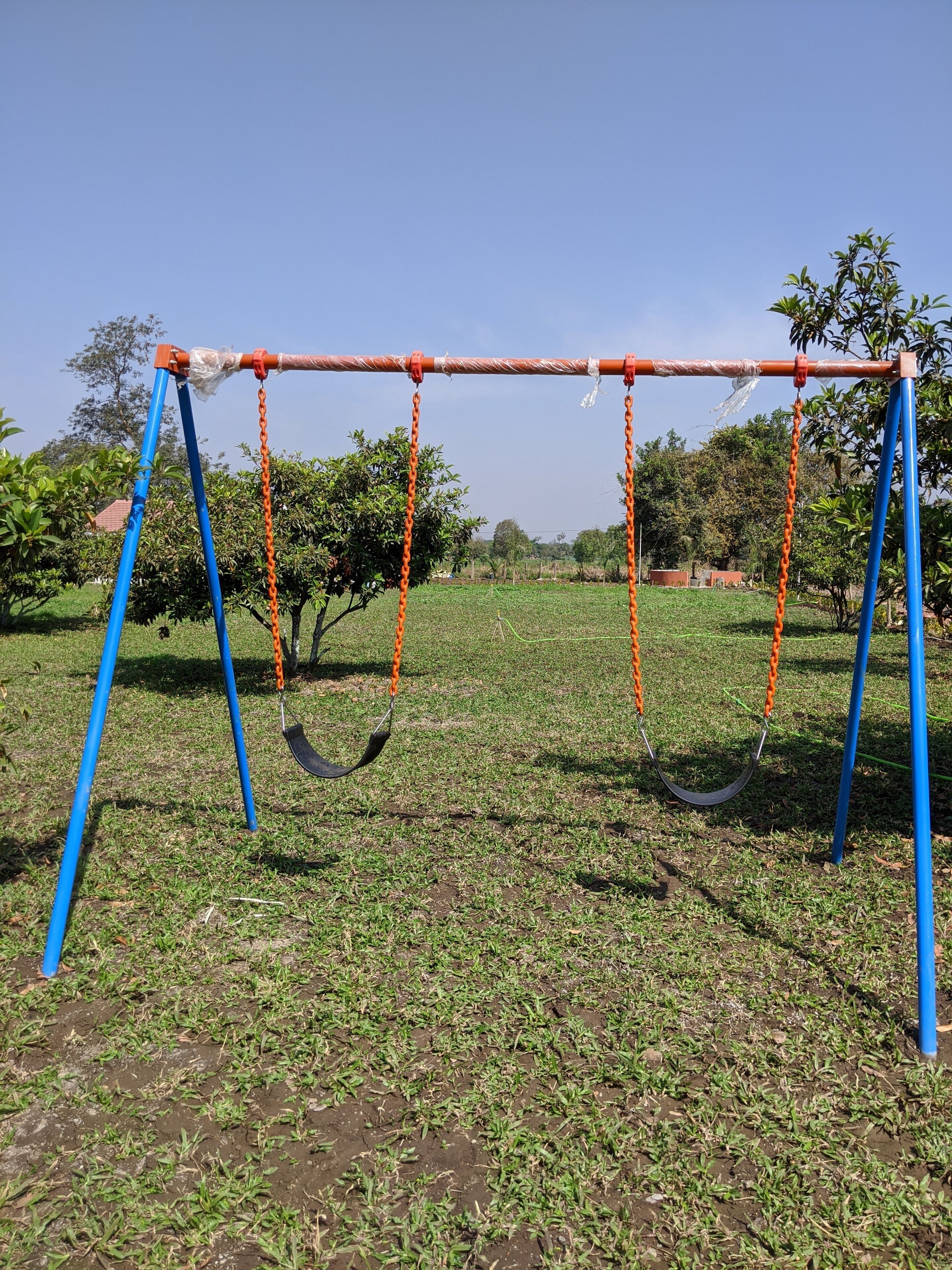 A swing set in a grassy field with trees in the background.
