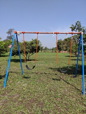 A swing set in a grassy field with trees in the background. - Mango Tree Farm (Karjat)