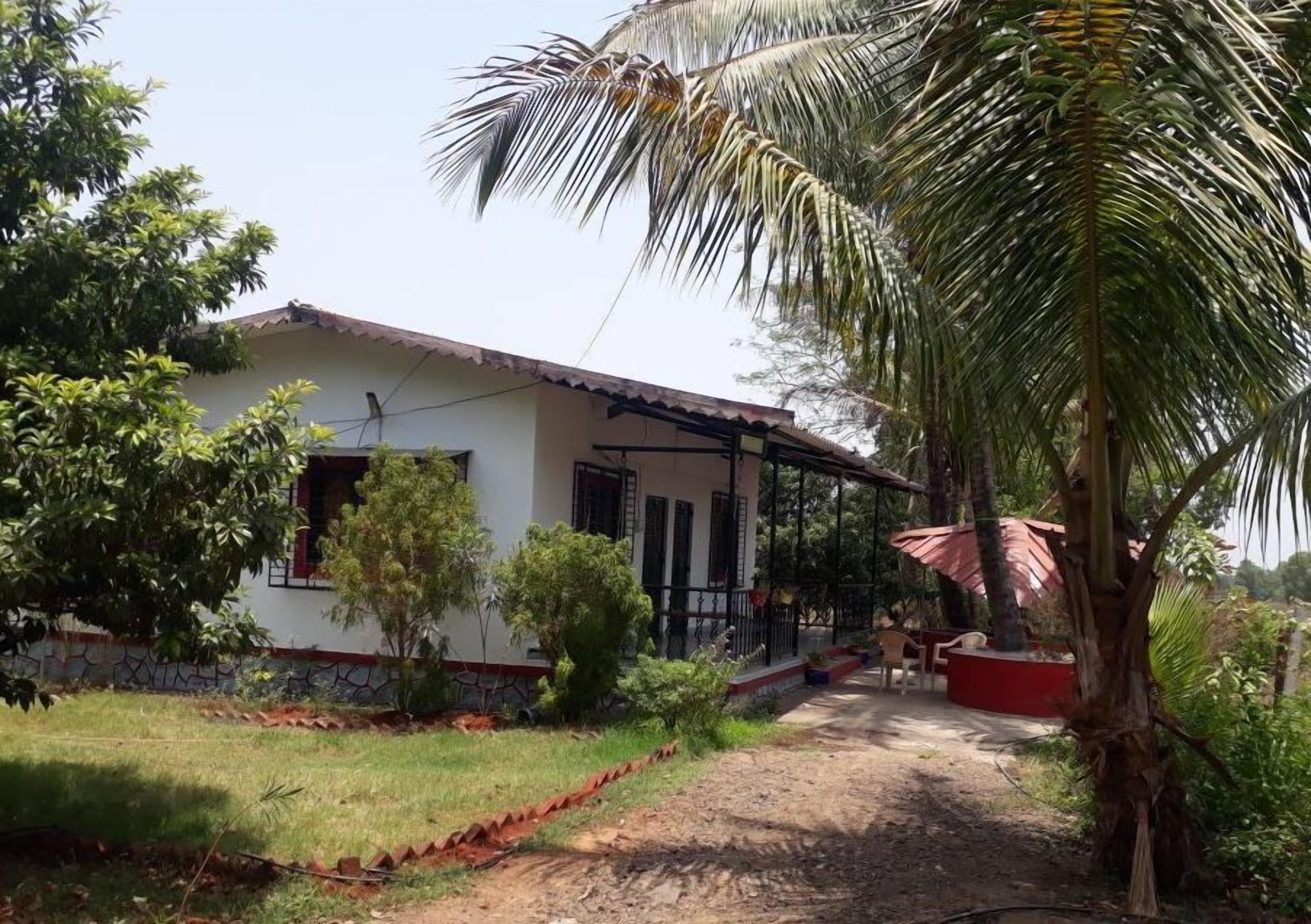 A house with a covered porch, a garden with various plants, and a dirt path leading to the entrance.