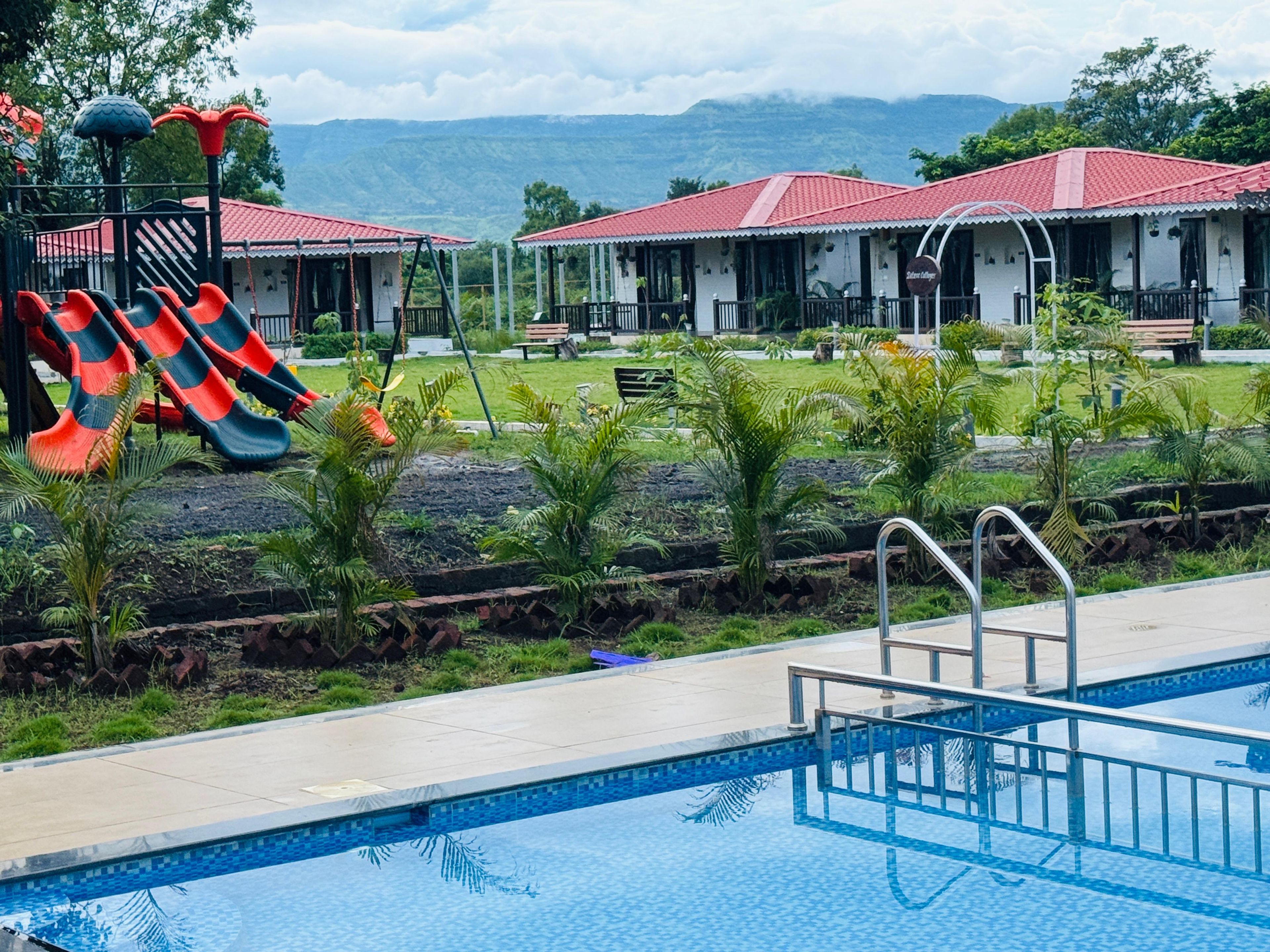 Piscina com escorrega, rodeada por um jardim e um edifício com telhado vermelho.