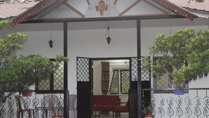 A traditional house with a tiled roof, a balcony with potted plants, and a red sofa inside. - Mango Tree Farm (Karjat)