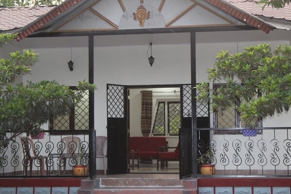 A traditional house with a tiled roof, a balcony with potted plants, and a red sofa inside. - Mango Tree Farm (Karjat)