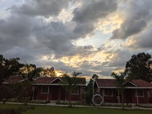 A row of red-roofed houses with a large wheel in the foreground, set against a cloudy sky. - Mango Tree Farm (Karjat)