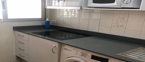 Una cocina compacta con microondas integrado, cocina y lavadora.