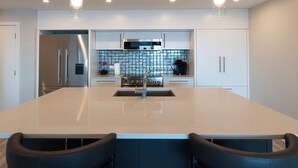 A modern kitchen with a central island, stainless steel appliances, and a tiled backsplash. - Otter Grotto (Victoria)