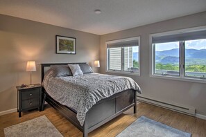 A bedroom with a bed, two bedside tables with lamps, a window with a view of mountains, and a framed picture on the wall. - Intervale Family Retreat: Mtn View & Pool Access! (Intervale)