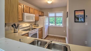Una cocina con armarios de madera, microondas, refrigerador, estufa y ventana con vistas al verdor.