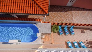 Vista aérea de un área de piscina en la azotea, con piscina azul, sillas de descanso y techo de azulejos.