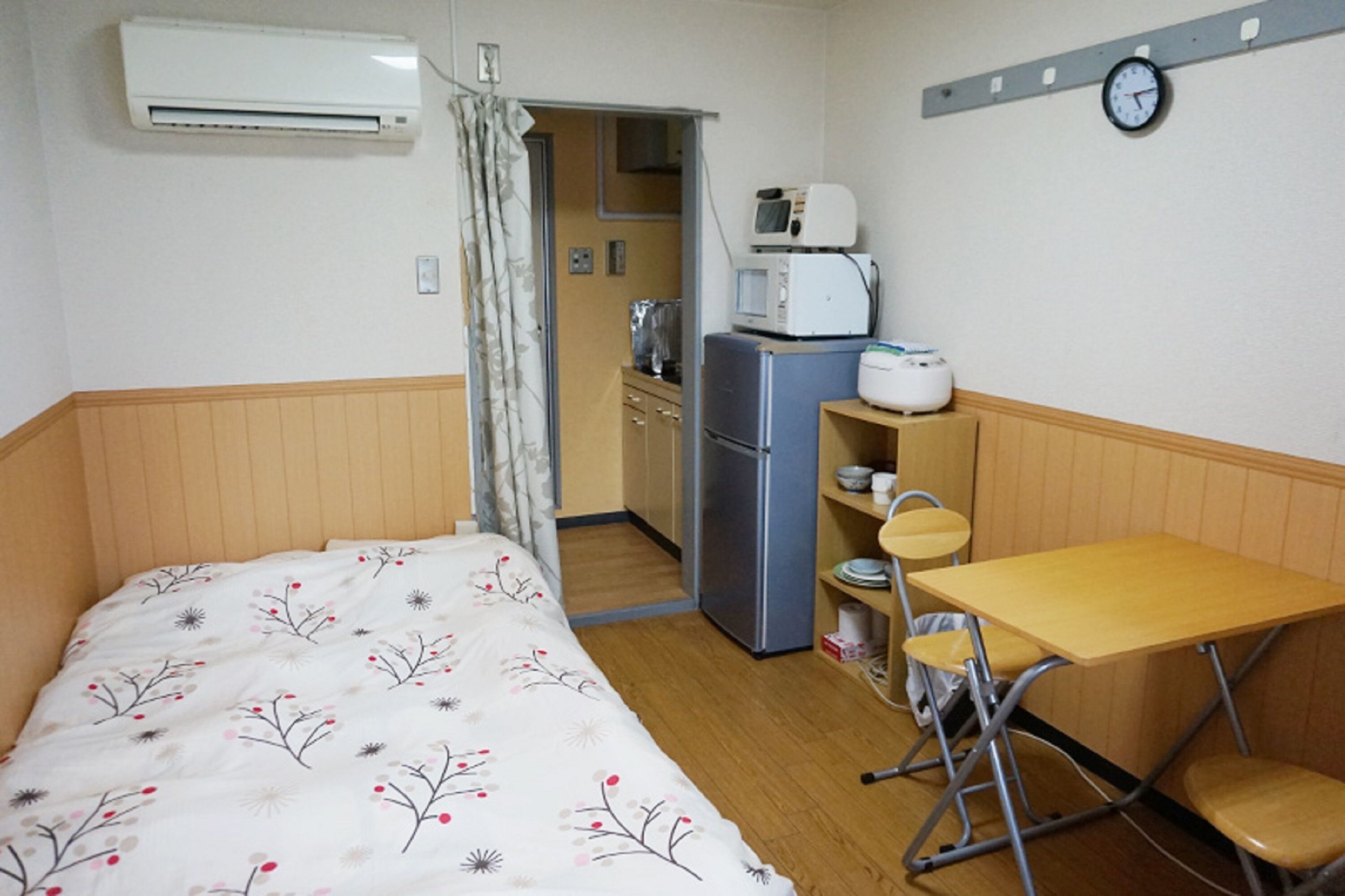 Ein kleines Zimmer mit Bett, einer Küchenzeile, einem Schreibtisch und einem Stuhl.