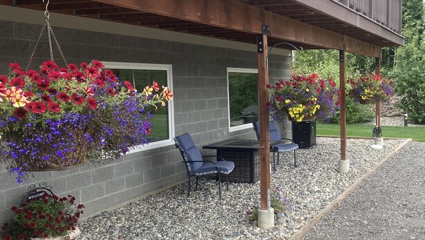 A covered outdoor seating area with chairs and tables, surrounded by flower planters and a gravel path. - Escape to Birchwood Suite (Fairbanks)