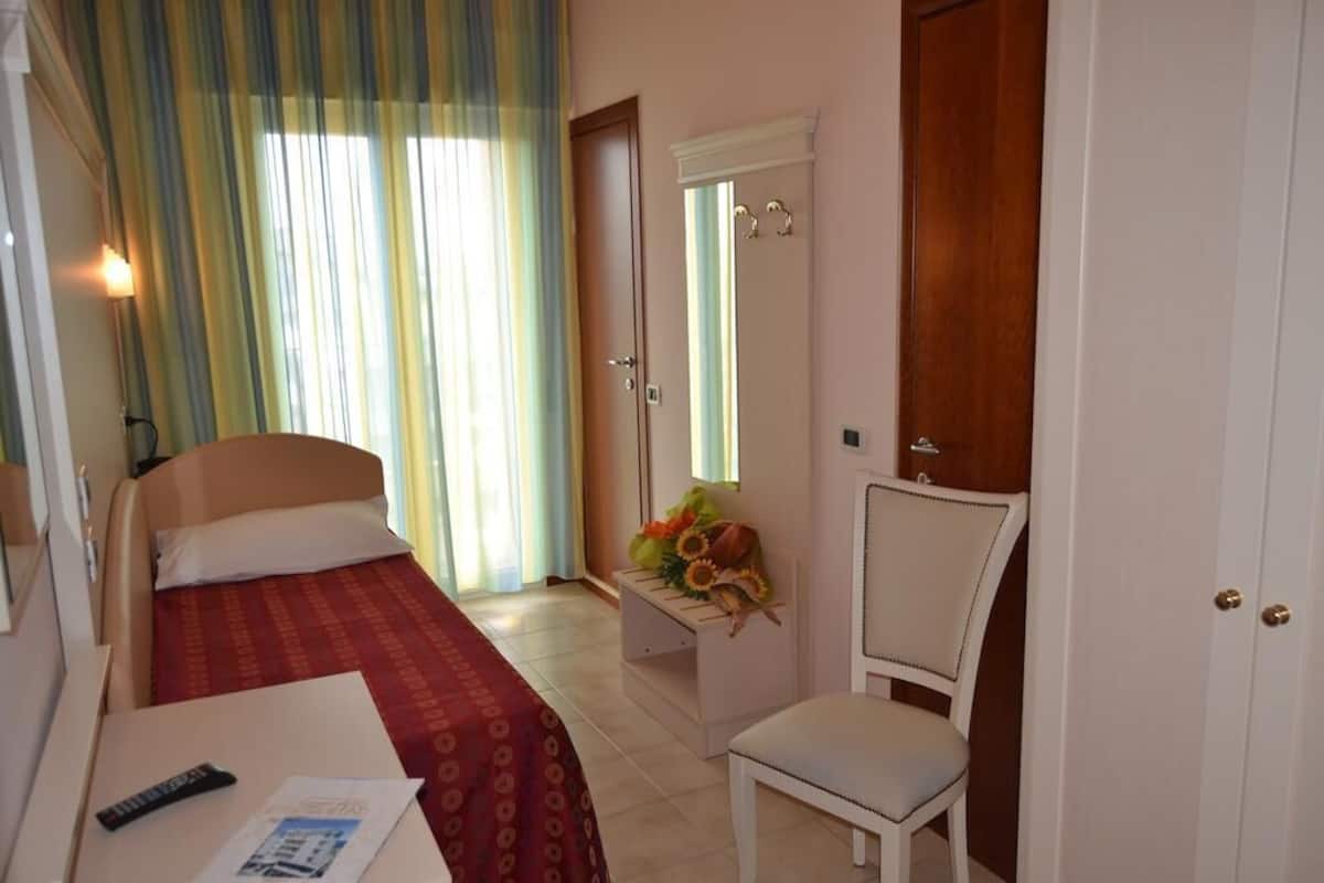 Una habitación de hotel con una cama, un escritorio, una silla y una pequeña mesa con un jarrón de flores.