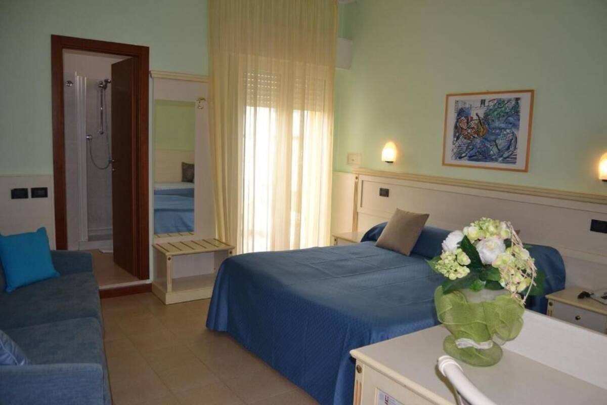 Una habitación de hotel con cama, sofá, ducha y un cuadro en la pared.