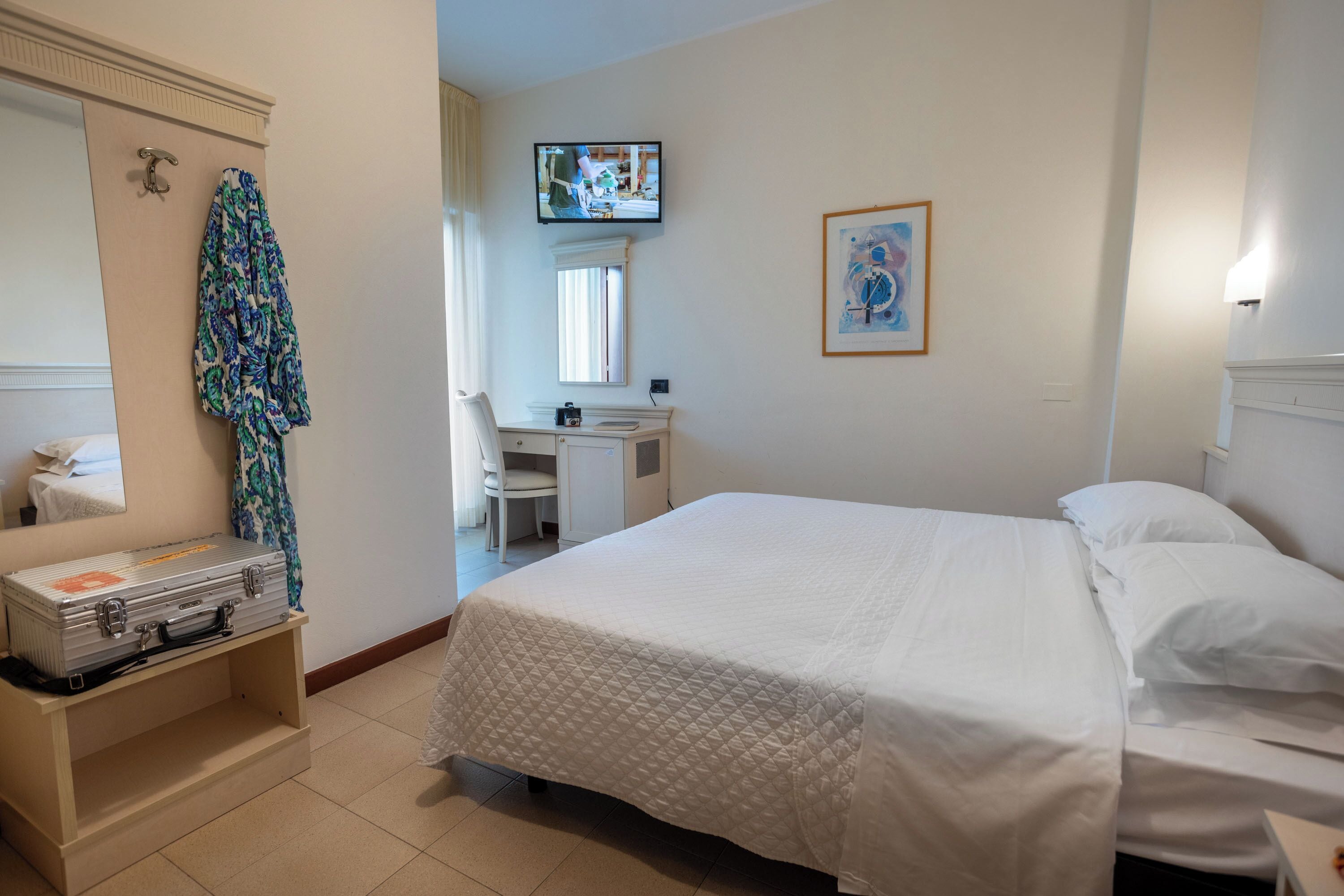 A hotel room with a bed, a desk, a chair, a television, and a framed picture on the wall.