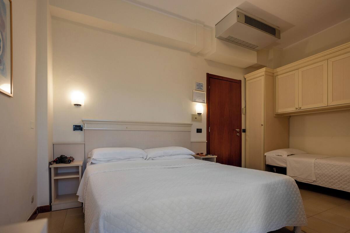 Un dormitorio con una cama grande, una mesita de noche, un armario y un aire acondicionado instalado en la pared.