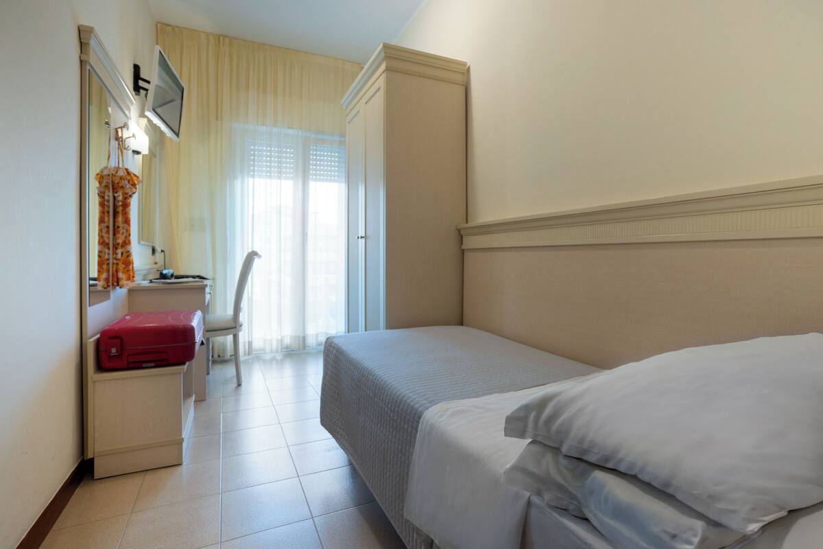 Habitación de hotel con cama, escritorio con silla, televisor montado en la pared y ventana con cortinas.